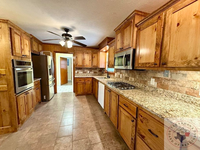 kitchen with ceiling fan, sink, light stone countertops, a textured ceiling, and stainless steel appliances