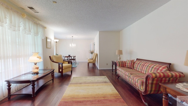 living area featuring a notable chandelier, visible vents, a textured ceiling, and wood finished floors