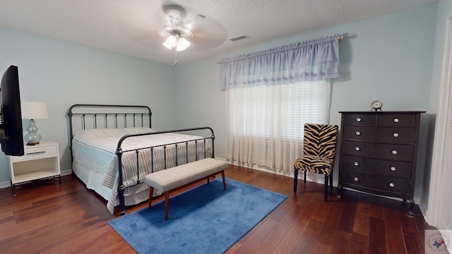 bedroom with a ceiling fan, baseboards, wood finished floors, visible vents, and a textured ceiling