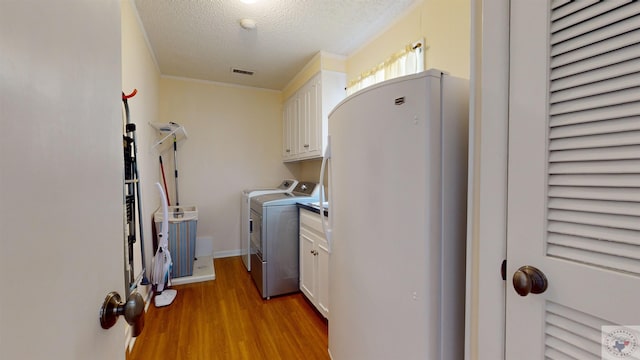 washroom with visible vents, light wood-style flooring, cabinet space, a textured ceiling, and washer and clothes dryer