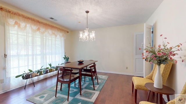 dining space with hardwood / wood-style floors, baseboards, visible vents, a textured ceiling, and a notable chandelier