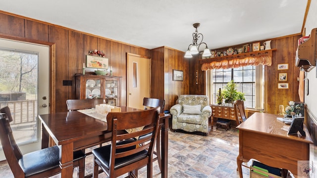 dining room with stone finish floor, an inviting chandelier, and wooden walls