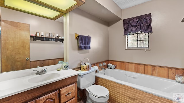 bathroom with a textured ceiling, a garden tub, toilet, a wainscoted wall, and vanity