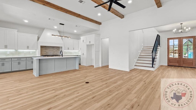 kitchen with tasteful backsplash, light wood-style flooring, custom range hood, beamed ceiling, and french doors