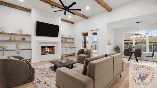 living area with a healthy amount of sunlight, light wood-style flooring, beamed ceiling, and a lit fireplace