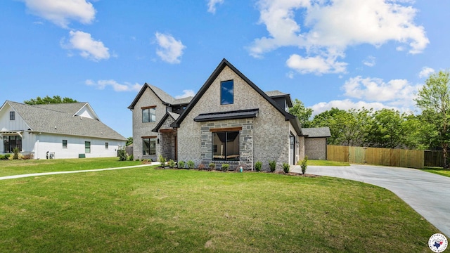 view of front of property featuring driveway, stone siding, a front yard, and fence