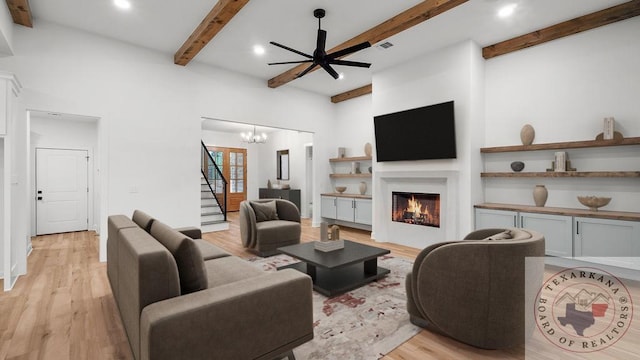 living room with stairway, a warm lit fireplace, light wood-style flooring, and beam ceiling