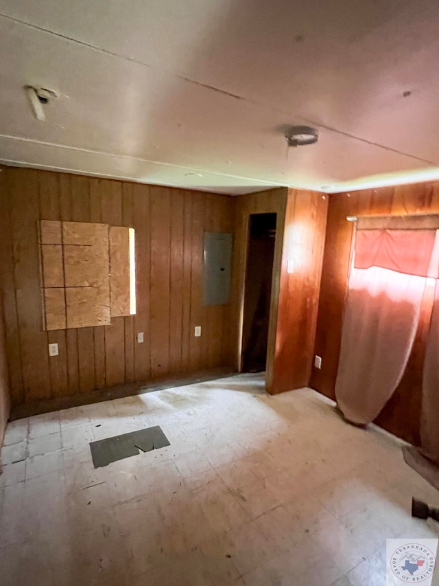 unfurnished room featuring light floors, electric panel, and wooden walls