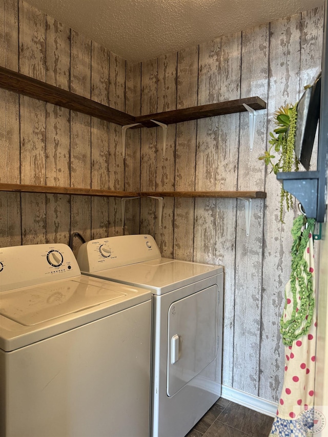 washroom with a textured ceiling, wooden walls, and washing machine and clothes dryer