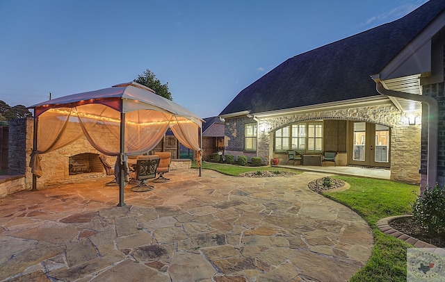 patio terrace at dusk featuring french doors and an outdoor stone fireplace