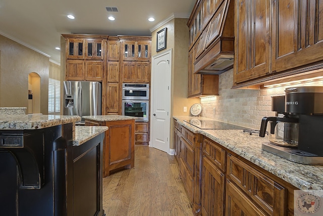 kitchen featuring stainless steel appliances, light stone counters, ornamental molding, and light hardwood / wood-style floors