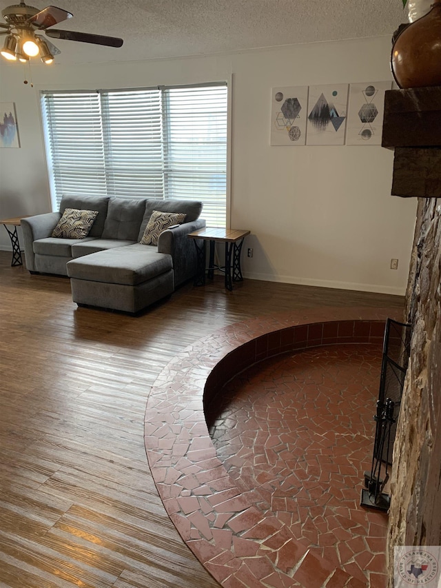 living area featuring baseboards, a ceiling fan, a textured ceiling, and wood finished floors