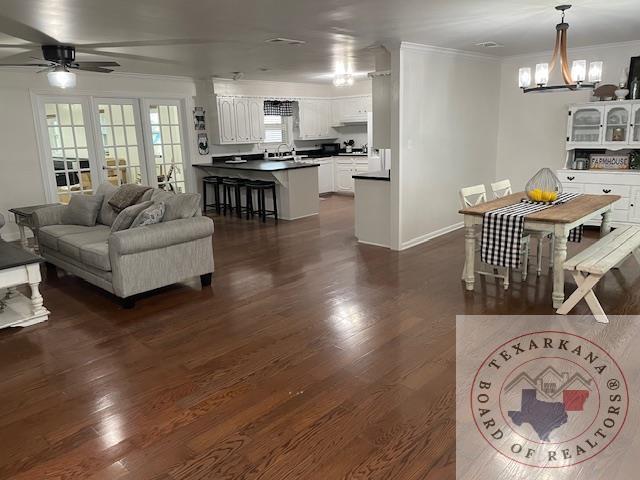 living room with ceiling fan with notable chandelier, dark wood-type flooring, and ornamental molding