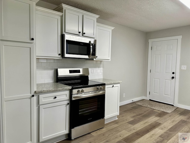 kitchen with light stone counters, white cabinets, tasteful backsplash, and appliances with stainless steel finishes