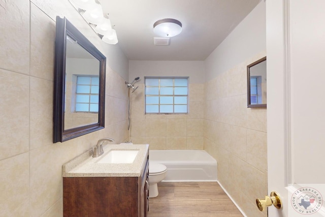 full bathroom with toilet, wood-type flooring, tile walls, vanity, and tiled shower / bath