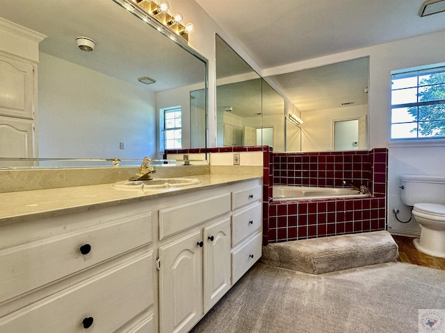 bathroom featuring vanity, toilet, a wealth of natural light, and tiled bath