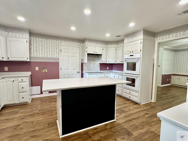 kitchen with hardwood / wood-style flooring, white cabinets, a center island, and white double oven