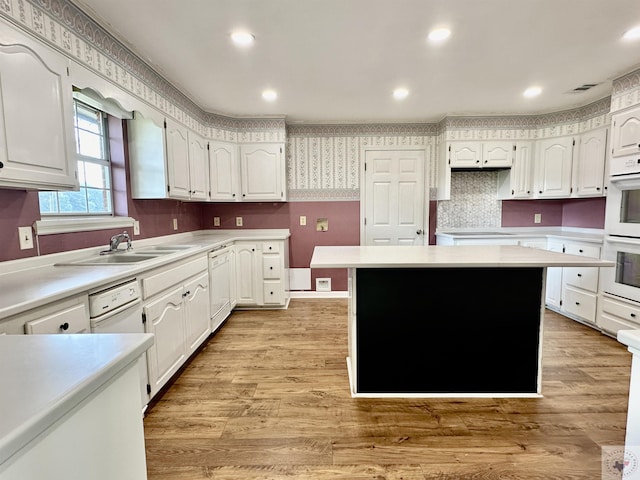 kitchen featuring white appliances, a kitchen island, white cabinetry, light hardwood / wood-style floors, and sink