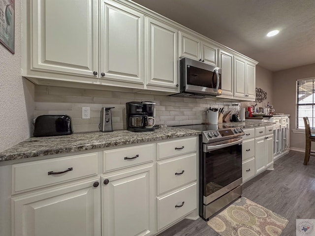 kitchen with white cabinetry, tasteful backsplash, light stone counters, appliances with stainless steel finishes, and hardwood / wood-style floors