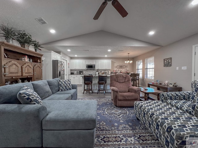 living room with ceiling fan with notable chandelier, wood-type flooring, vaulted ceiling, and a textured ceiling