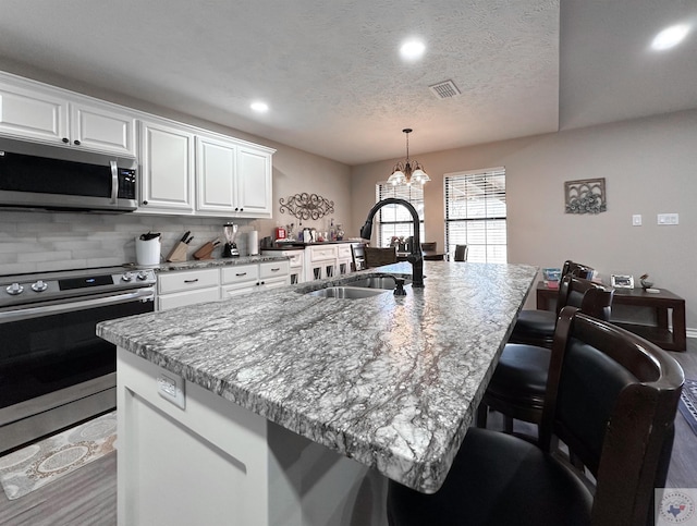 kitchen with white cabinetry, appliances with stainless steel finishes, a kitchen island with sink, and sink