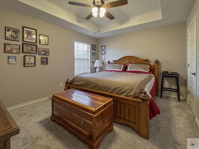 carpeted bedroom with a raised ceiling and ceiling fan