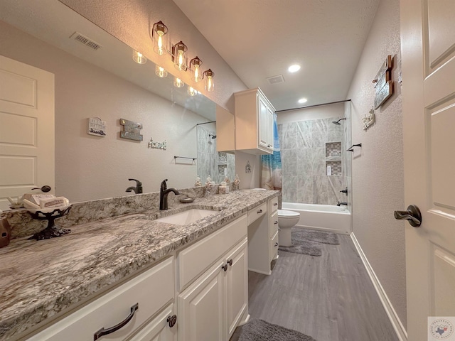 full bathroom with hardwood / wood-style flooring, tiled shower / bath, vanity, and toilet