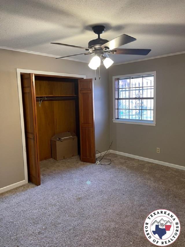 500 Wade Ln, Texarkana, TX 75501 - unfurnished bedroom with a textured ceiling, crown molding, a closet, baseboards, and light carpet