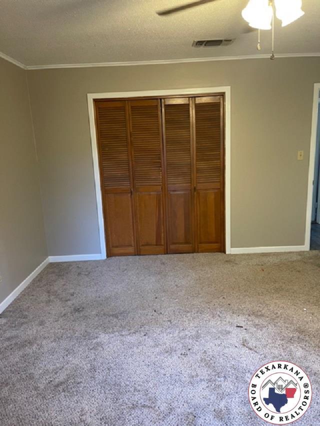 500 Wade Ln, Texarkana, TX 75501 - unfurnished bedroom featuring ornamental molding, a closet, baseboards, carpet, and a ceiling fan