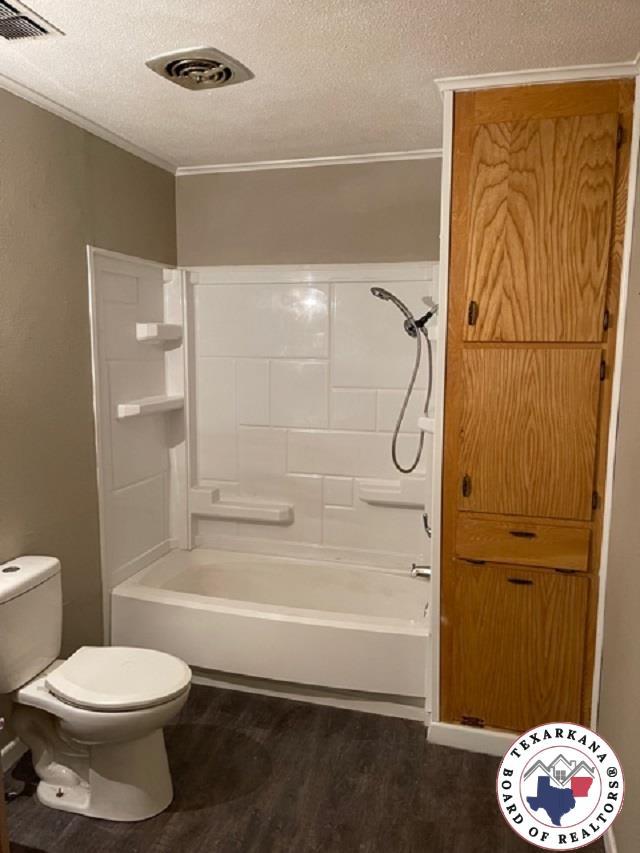 500 Wade Ln, Texarkana, TX 75501 - full bathroom featuring wood finished floors, ornamental molding, a textured ceiling, toilet, and bathing tub / shower combination