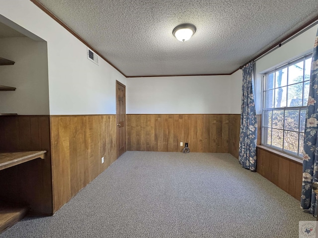 spare room featuring carpet, wooden walls, a textured ceiling, and ornamental molding