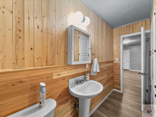 bathroom featuring a textured ceiling, hardwood / wood-style floors, wooden walls, toilet, and ornamental molding