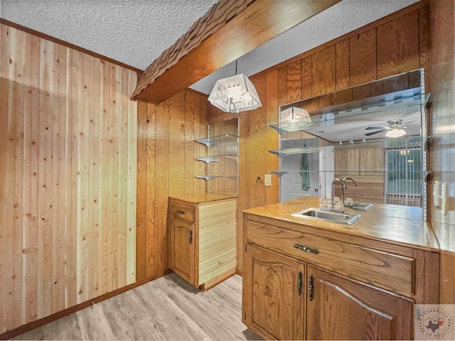 kitchen featuring beamed ceiling, a textured ceiling, sink, light wood-type flooring, and wood walls