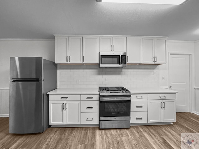 kitchen with white cabinetry, stainless steel appliances, tasteful backsplash, ornamental molding, and light hardwood / wood-style flooring