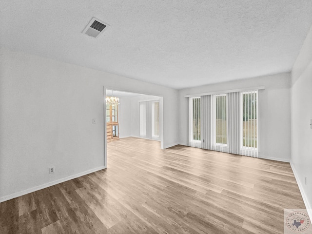 empty room featuring a notable chandelier, light wood-type flooring, and a textured ceiling