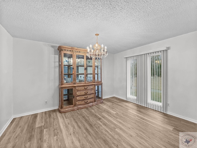 unfurnished dining area with a textured ceiling, wood-type flooring, and a chandelier