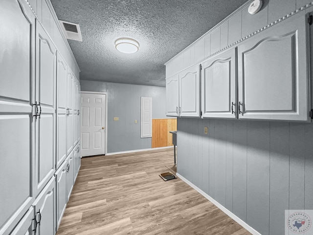 clothes washing area with a textured ceiling, light hardwood / wood-style flooring, and wood walls