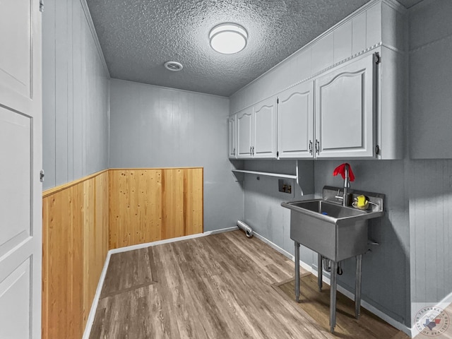 laundry room with a textured ceiling, cabinets, wooden walls, light hardwood / wood-style floors, and washer hookup