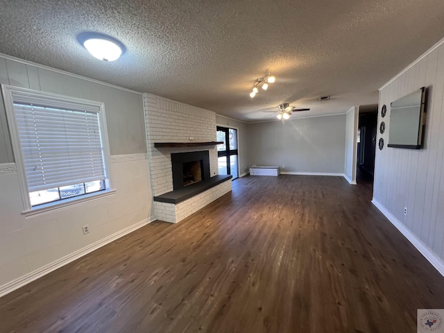 unfurnished living room with dark wood-type flooring, crown molding, a fireplace, and ceiling fan