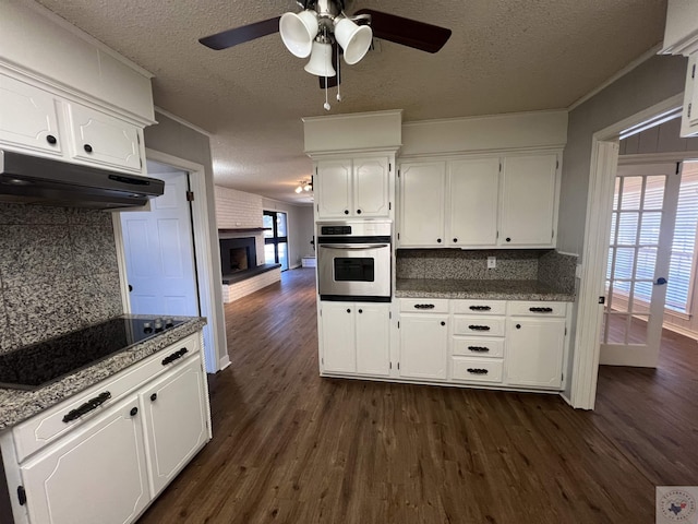 kitchen with oven, black electric stovetop, under cabinet range hood, and dark wood finished floors