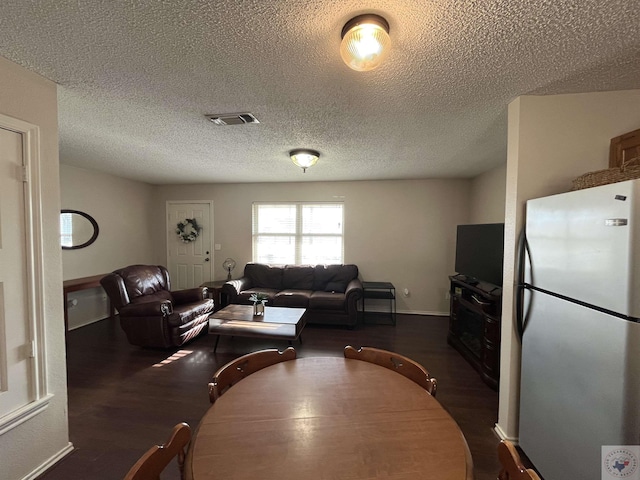 living area featuring a textured ceiling, dark wood-style flooring, visible vents, and baseboards