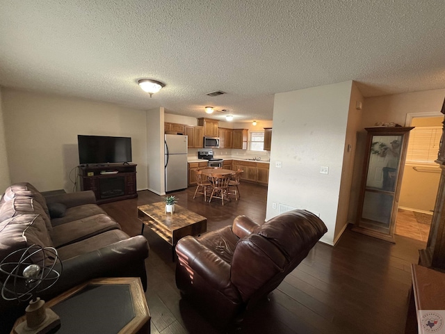 living room featuring visible vents, dark wood finished floors, a textured ceiling, and baseboards