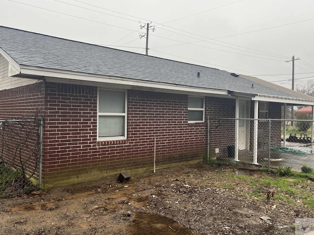 view of home's exterior featuring a shingled roof, brick siding, and fence