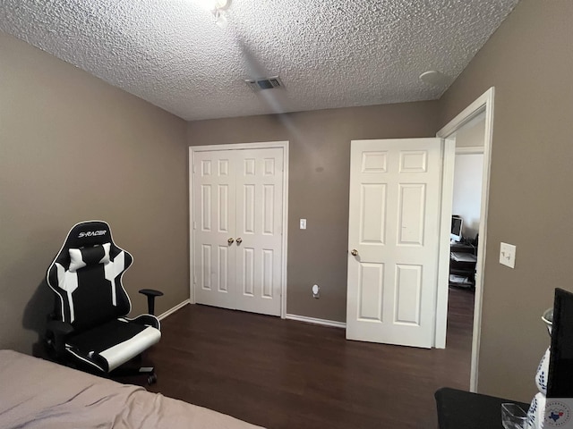 unfurnished bedroom with a textured ceiling, visible vents, baseboards, a closet, and dark wood finished floors