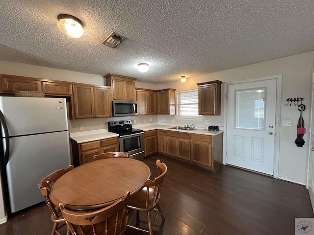 kitchen with visible vents, brown cabinetry, appliances with stainless steel finishes, dark wood-type flooring, and light countertops