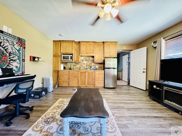 kitchen with radiator heating unit, stainless steel appliances, light hardwood / wood-style floors, backsplash, and ceiling fan