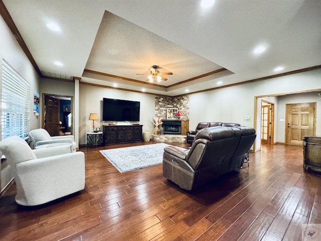 living room with crown molding, a fireplace, a textured ceiling, dark hardwood / wood-style floors, and a tray ceiling