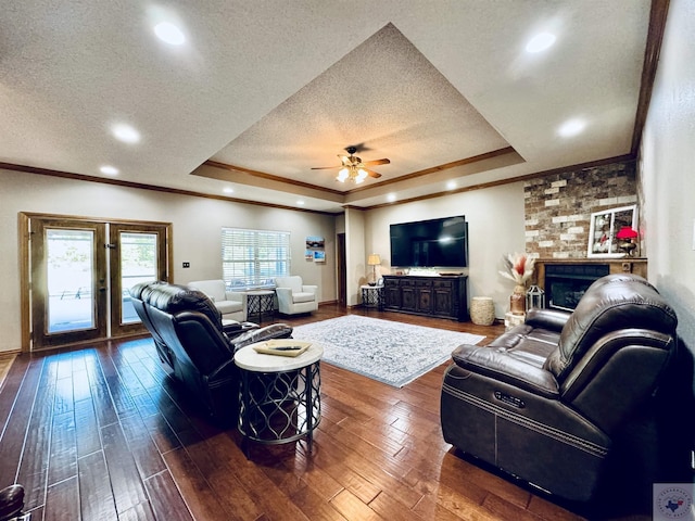 living room with crown molding, a brick fireplace, a tray ceiling, and dark hardwood / wood-style flooring