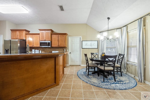 kitchen featuring vaulted ceiling, a textured ceiling, decorative backsplash, decorative light fixtures, and stainless steel appliances