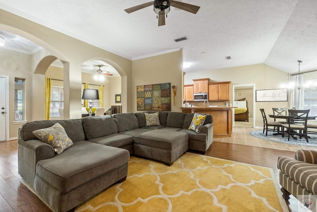 living room featuring ceiling fan with notable chandelier, a textured ceiling, light hardwood / wood-style floors, ornamental molding, and vaulted ceiling